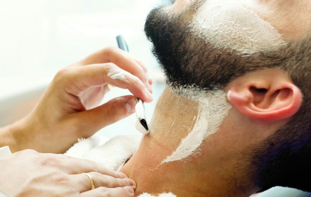 Barber shaving customer with straight razor in barbershop